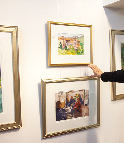 closeup of art curator's hand as she adjusts two paintings being exhibited using an art gallery hanging system