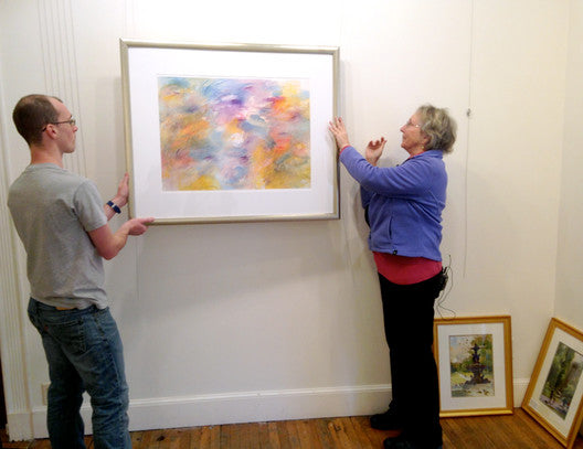 painting being hung using picture hanging system by man and woman, workers at an art gallery