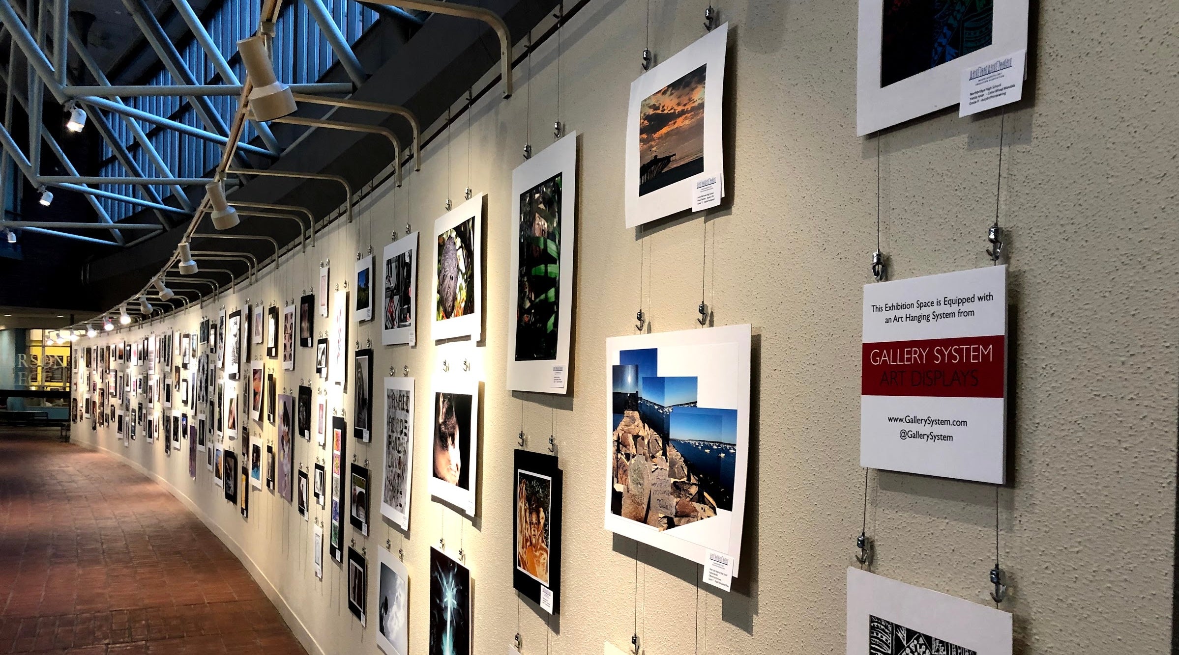 unframed student artworks displayed on art hanging system at public building in Boston