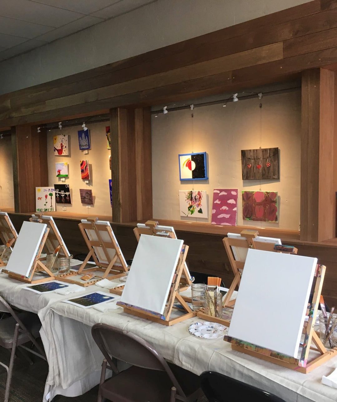 paintings shown in wall alcoves on art gallery hanging system with integrated art lighting, with table set up for art class