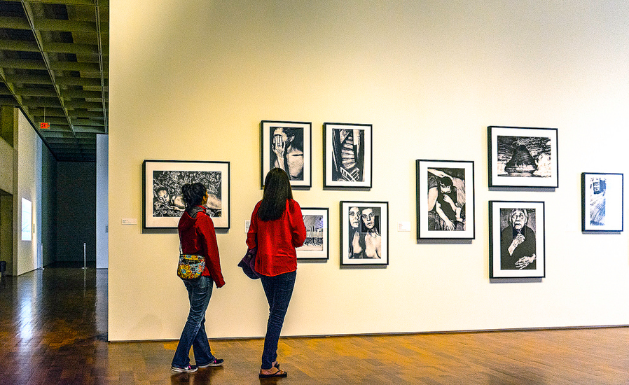 artfully arranged group of prints on art gallery wall, being observed by two women