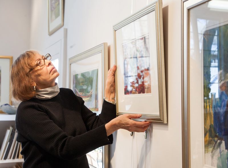artist hanging a painting using a wall mounted art gallery hanging system in her studio
