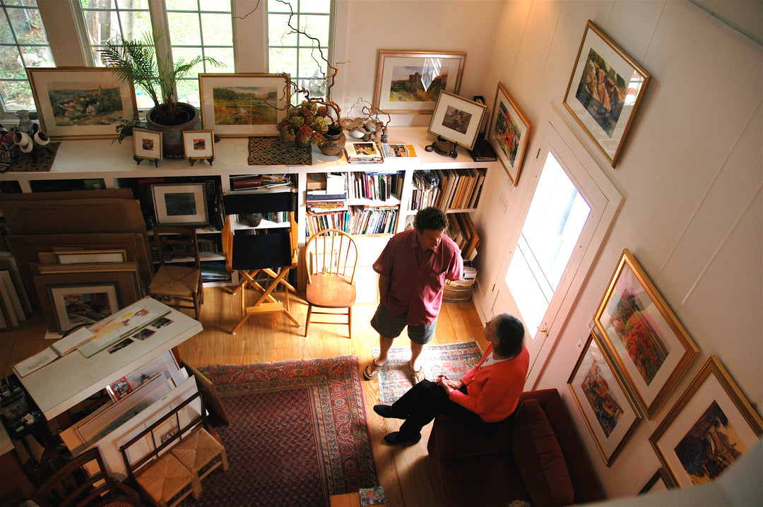 view looking down into an artist's studio with multiple paintings on walls displayed on a picture hanging system