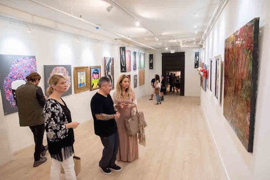 loft-style art gallery interior, showing visitors looking at large paintings displayed on picture hanging systems with integrated art gallery lighting