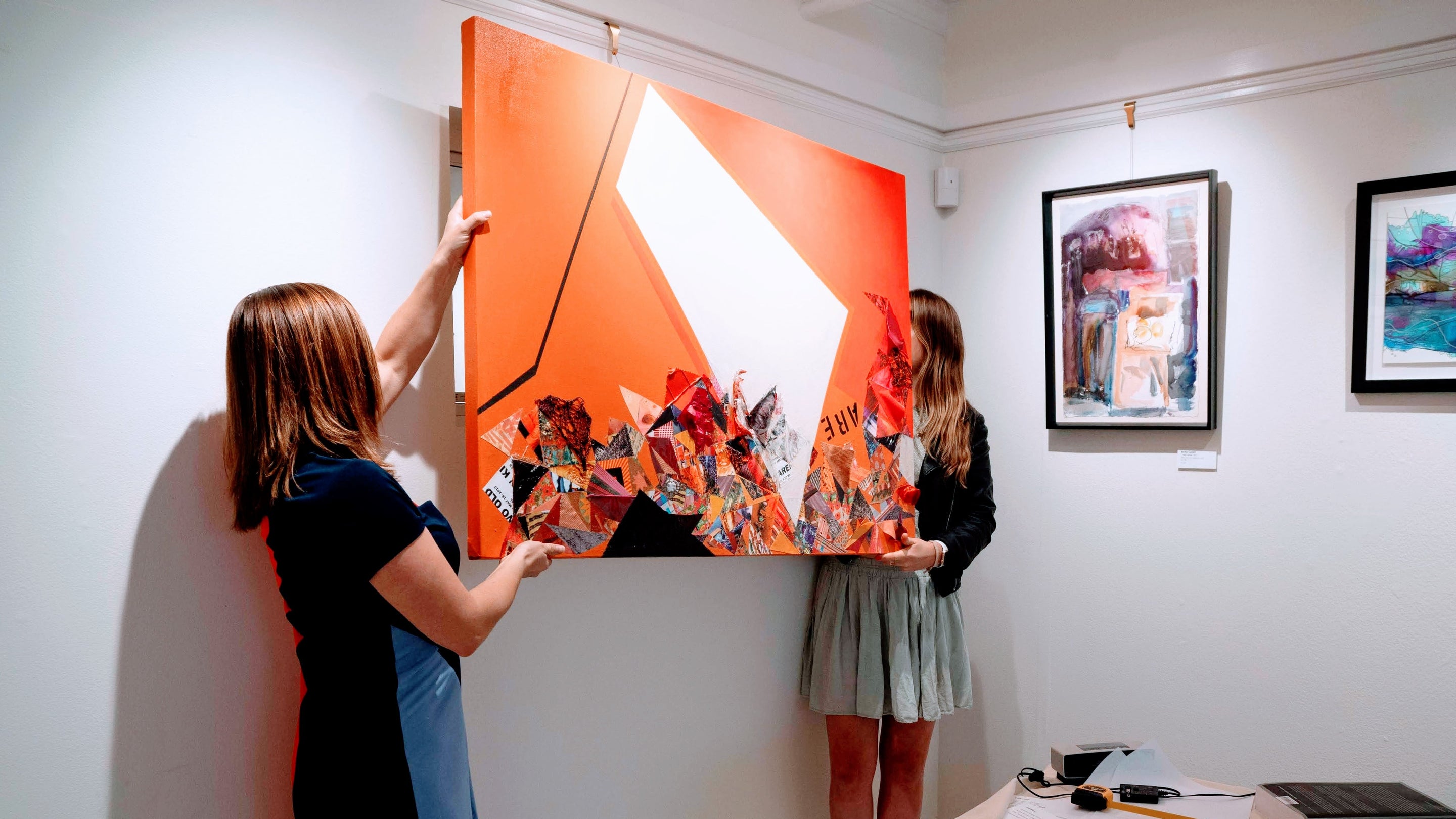 two art gallery curators raising a painting into place for hanging on picture rail molding hangers