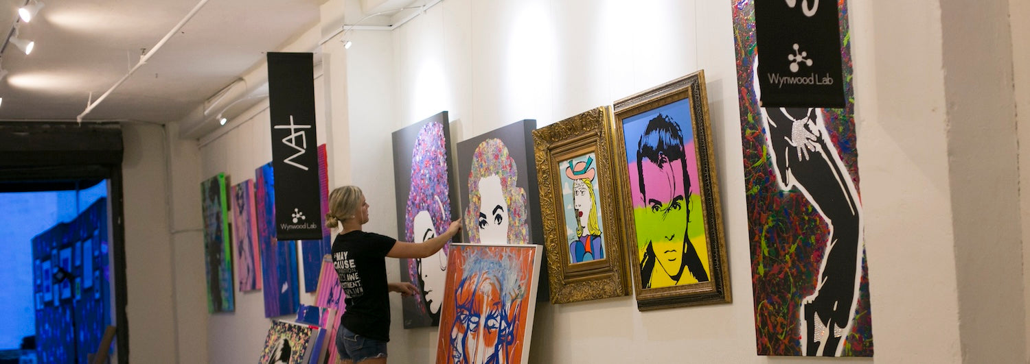 woman hanging artworks at an art gallery, using a wall mounted picture hanging system with integrated art lighting