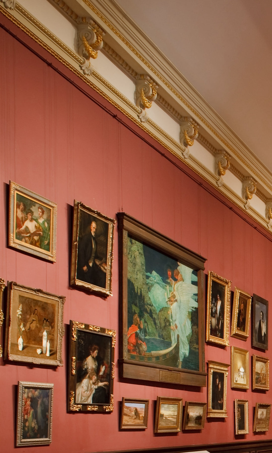 About 20 paintings displayed in a salon-style grouping, hung on a gallery art hanging system