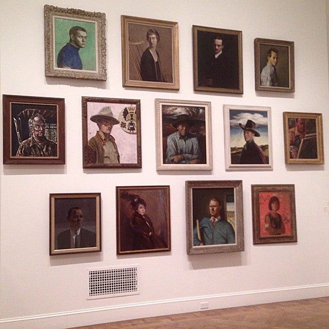 gallery wall display of 13 painted portraits in three rows at art gallery