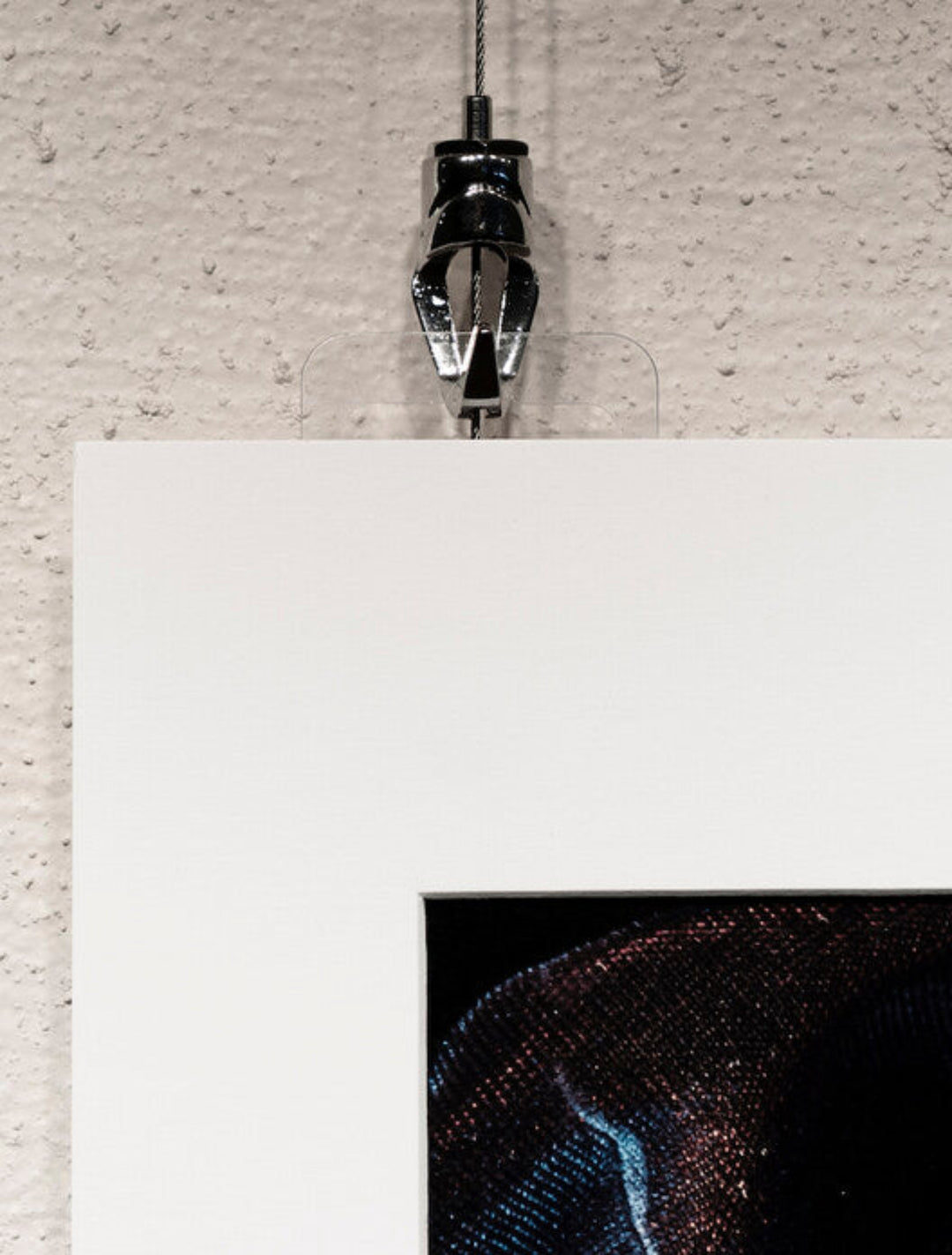 clear plastic tab hanger being used to hold matted but unframed artwork on art gallery hanging system