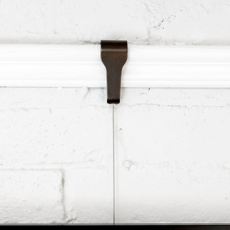 Front view of Bronze picture rail molding hook for art hanging, shown in use on white wall
