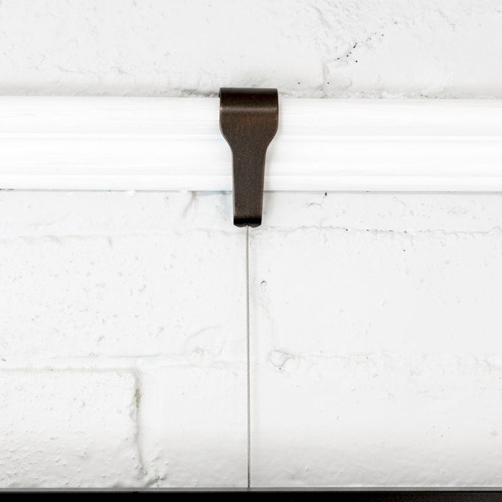 Front view of Bronze picture rail molding hook for art hanging, shown in use on white wall