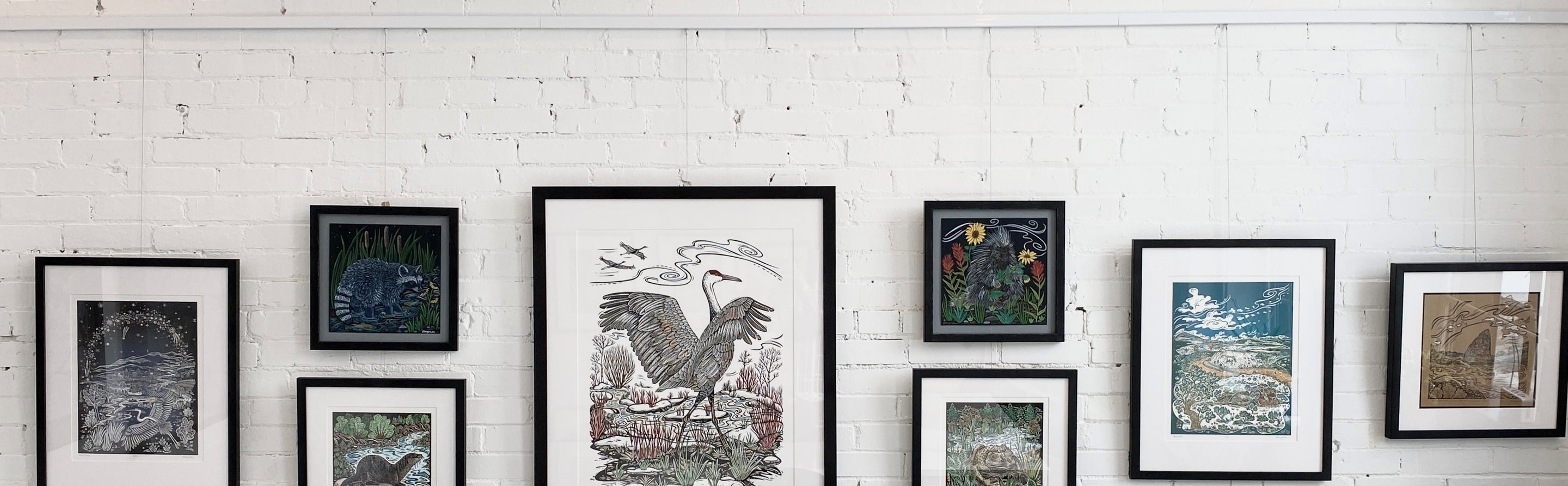 seven prints of different sizes displays against white bricks using wall mounted art gallery hanging system