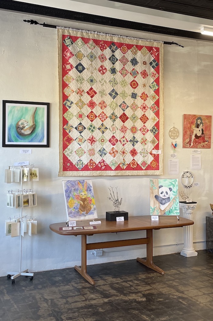 Interior of art gallery with picture hanging system, quilt and paintings on display