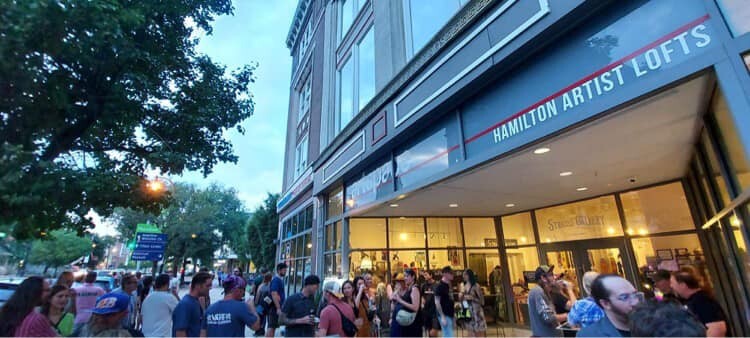 Exterior of Strauss Gallery with crowd on sidewalk for art show on picture hanging system