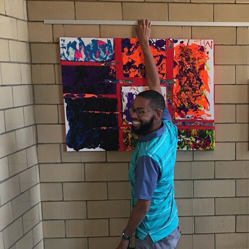 Teacher on ladder hanging student art in stairwell, using art hanging system